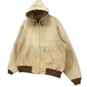 May include: A tan Carhartt hooded jacket with a brown zipper and brown trim around the bottom. The jacket has a patch on the left chest with the Carhartt logo.