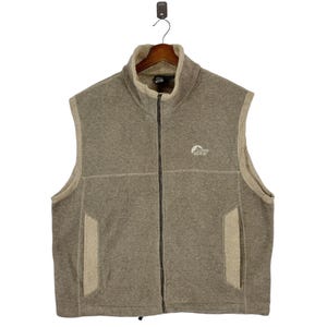 May include: A brown fleece vest with a zipper closure and a logo that says "Alpine Design" on the left chest. The vest has two pockets on the sides.