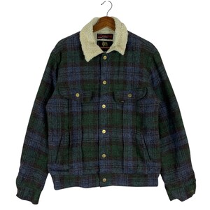 以下が含まれることがあります： 緑と青の色合いのチェック柄ジャケット。クリーム色のふわふわの襟が付いています。ジャケットには金色のボタンと2つの胸ポケットが付いています。「Lee」のブランド名がジャケットに表示されています。