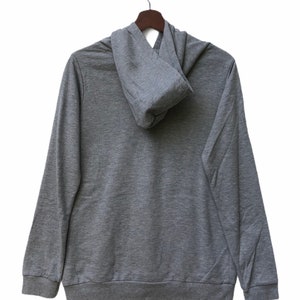May include: A gray hooded sweatshirt with a zipper closure. The hoodie is folded down and the sweatshirt is hanging on a wooden hanger.