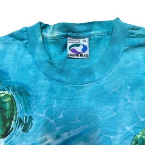 May include: A turquoise XL Liquid Blue t-shirt featuring a sea turtle design. The shirt has a tie-dye effect with a crew neck and a Liquid Blue tag. The shirt is made of 100% cotton.