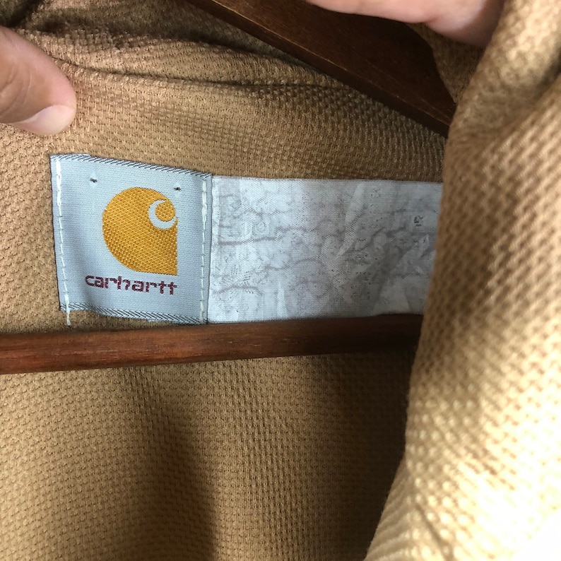 May include: A brown Carhartt workwear jacket with a white label that says "carhartt" in black lettering.