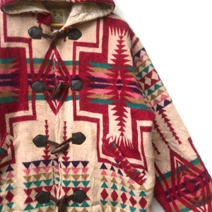 May include: A beige and red patterned duffle coat with a hood. The coat features a geometric design in red, green, pink, and purple. It has leather toggles and a button closure. The coat is made of a thick, warm material.