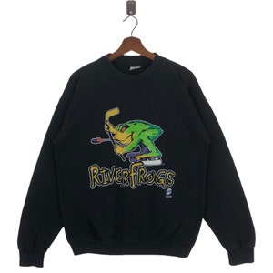 May include: Black sweatshirt with a green frog wearing ice skates and holding a hockey stick. The frog is in front of the text "RiverFrogs".