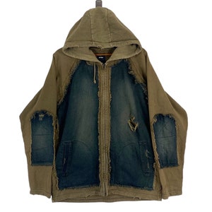 Puede incluir: Una sudadera con capucha marrón con cierre de cremallera. La sudadera ha sido remendada con tela vaquera y tiene detalles desgastados.