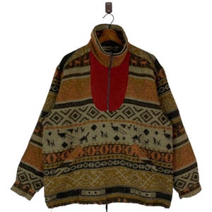 Puede incluir: Un jersey de polar de color marrón, naranja y rojo con cierre de media cremallera. El polar tiene un patrón geométrico con figuras de animales.