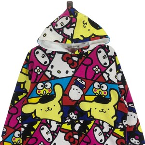 Op de afbeelding: Een kleurrijk hooded sweatshirt met een patchwork ontwerp met verschillende cartoonfiguren, waaronder Hello Kitty, My Melody en Keroppi. Het sweatshirt is gemaakt van een zachte, comfortabele stof en heeft een ontspannen pasvorm.