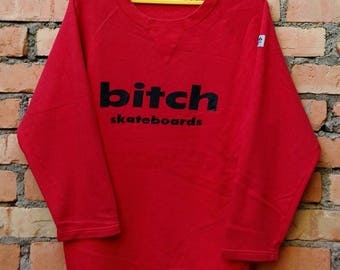 May include: Red long-sleeve sweatshirt with the text "bitch skateboards" printed in black on the front.