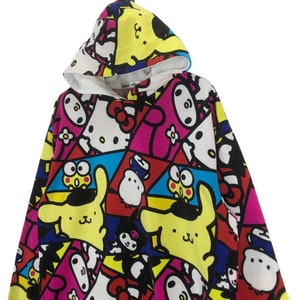 Op de afbeelding: Een kleurrijk hoodie met een veelkleurige print met Hello Kitty en andere cartoonfiguren. De print bevat geel, roze, blauw, rood en zwart.