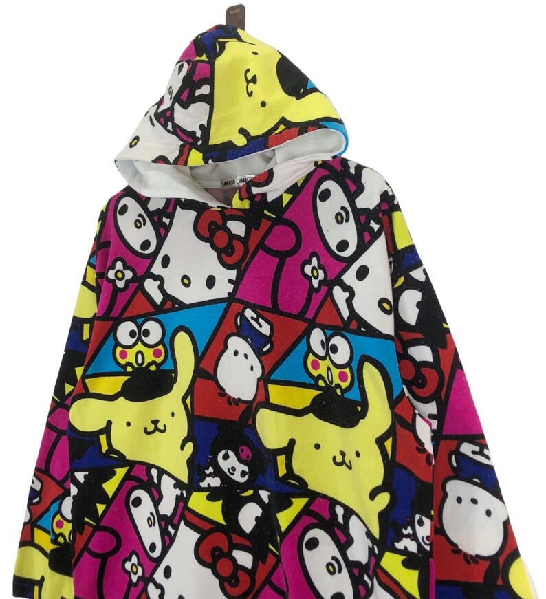 Op de afbeelding: Een kleurrijk hoodie met een veelkleurige print met Hello Kitty en andere cartoonfiguren. De print bevat geel, roze, blauw, rood en zwart.