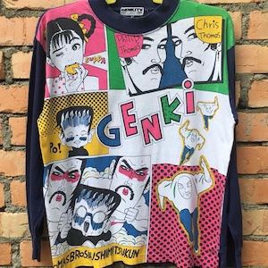 May include: A blue long-sleeve shirt with a colorful cartoon print. The shirt features a variety of characters, including a girl eating a sandwich, a man with a mustache, and a man with a beard. The shirt also features the word "GENKI" in large, bold letters.