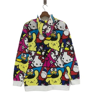 Op de afbeelding: Een wit hoodie met een kleurrijke all-over print met cartoonfiguren. De print bevat de kleuren geel, roze, blauw, rood, zwart en groen. De personages zijn een konijn, een kat en een kikker.