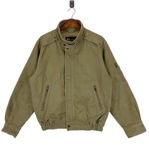 May include: A green canvas jacket with a zipper closure, a stand-up collar, and multiple pockets. The jacket has a drawstring at the waist.