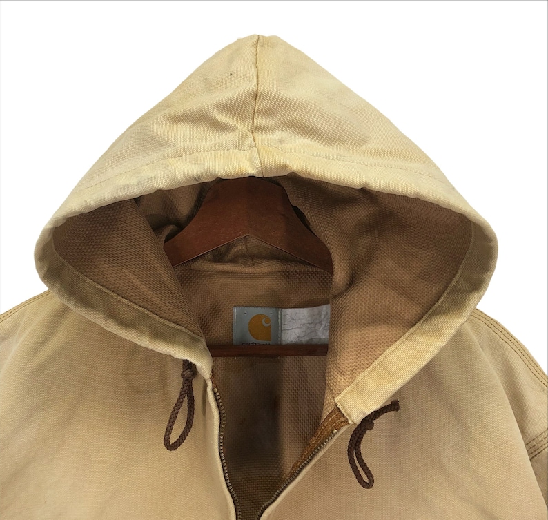 May include: A tan Carhartt hooded jacket with a zipper closure and a brown drawstring. The jacket has a brown label with the Carhartt logo on the front.