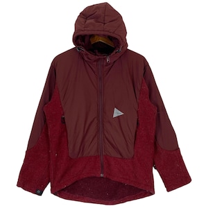 May include: A burgundy hooded jacket with a zipper closure and a small triangular logo on the left chest. The jacket is made of a combination of fleece and quilted fabric.