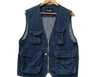 May include: A blue denim vest with multiple front pockets and a silver zip closure. The vest has a V-neck design and is hanging on a wooden hanger against a white background. The vest has the brand name "Abaraya" on the label.