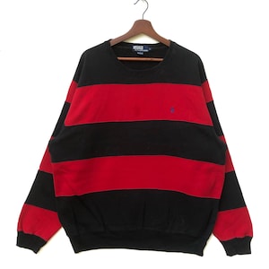 May include: Black and red striped sweatshirt with a small blue polo player logo on the chest. The sweatshirt has a crew neck and long sleeves.