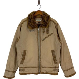 Puede incluir: Una chaqueta marrón con cremallera, cuello de piel sintética y detalles en cuero marrón. La chaqueta tiene cierre de cremallera y dos bolsillos en la parte delantera. El nombre de la marca "VOLLDOR" es visible en la etiqueta.