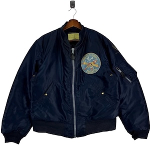 May include: A dark navy blue bomber jacket featuring a front zip fastening, ribbed cuffs and hem, and a circular embroidered patch on the chest depicting a yellow aeroplane with the text 6147 T.C.S. KOREA MOSQUITO.