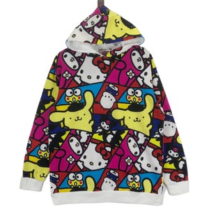 Op de afbeelding: Een wit hoodie met een kleurrijke all-over print met cartoonfiguren zoals Hello Kitty en My Melody. De print is een mix van roze, geel, blauw, rood en zwart.