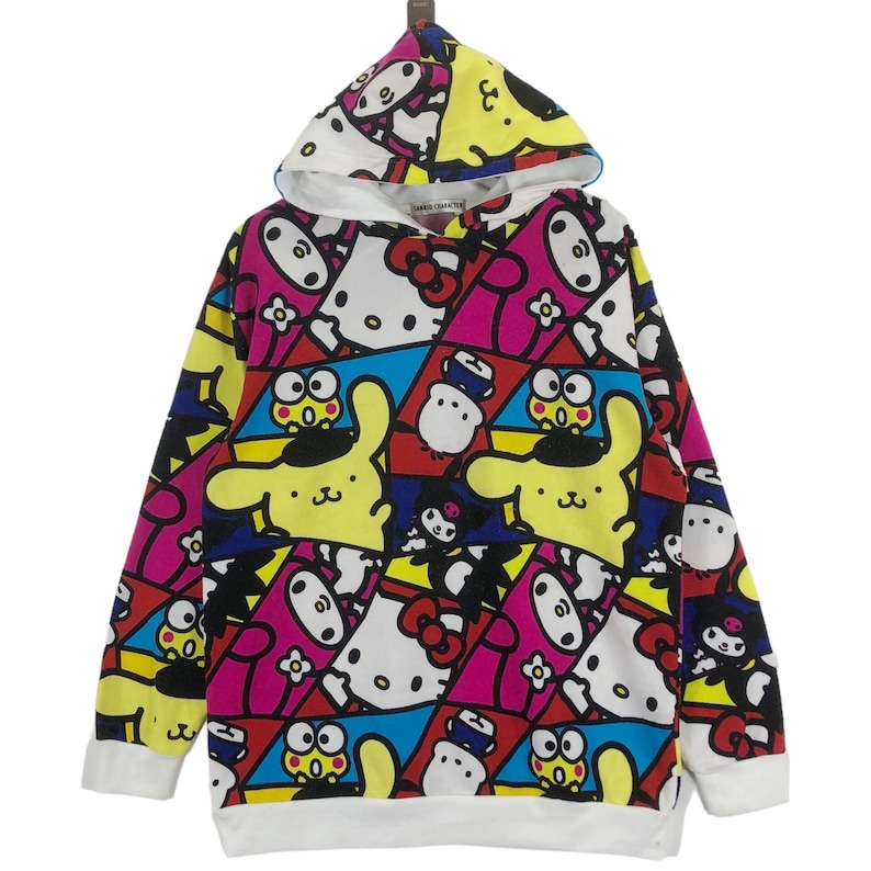 Op de afbeelding: Een wit hoodie met een kleurrijke all-over print met cartoonfiguren zoals Hello Kitty en My Melody. De print is een mix van roze, geel, blauw, rood en zwart.