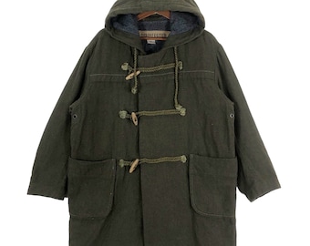 Könnte beinhalten: Ein dunkelgrüner Kapuzen-Dufflecoat mit Knöpfen und zwei großen Taschen. Der Mantel hat ein Etikett mit der Aufschrift "DISINFECTED".