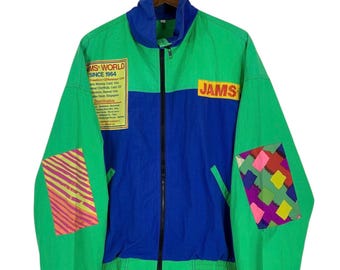 May include: A green and blue zip-up jacket featuring a high collar, a black front zipper, and the text JAMS WORLD SINCE 1964 on a yellow patch. The sleeves have colorful patterned rectangular patches, and the word JAMS is printed in yellow.