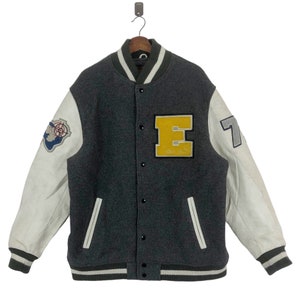 May include: A gray and white varsity jacket with leather sleeves. The jacket has a yellow "E" patch on the front and a white "7" on the right sleeve.