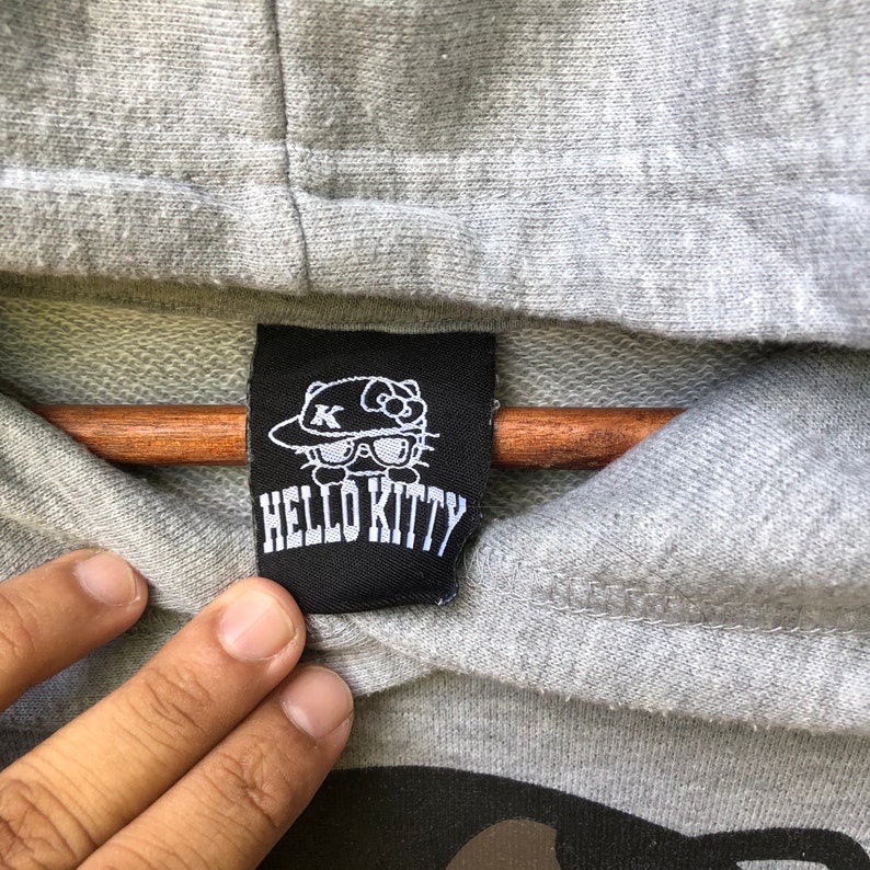 May include: A black and white Hello Kitty label with a cartoon image of Hello Kitty wearing a hat and sunglasses. The label says "Hello Kitty" in white letters.
