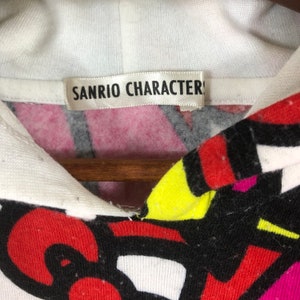 Op de afbeelding: Witte hoodie met een kleurrijke abstracte print en een label met de tekst "Sanrio Characters".