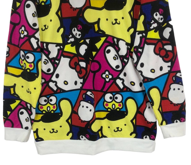 Op de afbeelding: Een wit longsleeve sweatshirt met een kleurrijke all-over print met cartoonfiguren zoals Hello Kitty, My Melody en Keroppi.