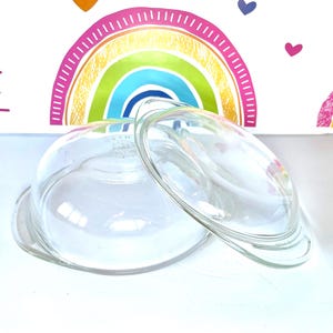 Puede incluir: Dos tapas de vidrio transparente para una fuente para hornear. Las tapas son redondas y tienen un borde ligeramente elevado.