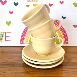 May include: A white ceramic mug with a black handle and the text "But First, Coffee" in a handwritten style. The mug is on a white surface. The mug is 4 inches tall.