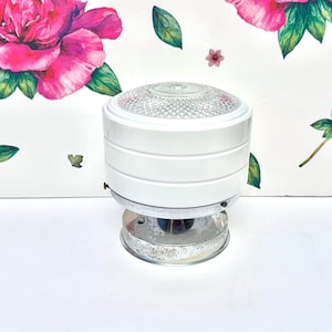 May include: A cylindrical ceiling light fixture featuring a white metal body with horizontal grooved detailing. The top is capped with a clear, textured glass lens with a diamond pattern, while the base is a circular, reflective chrome-finished metal plate.