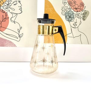 May include: A vintage glass coffee carafe with a black handle and lid, and gold accents. The carafe has a starburst pattern and is approximately 20 cm tall. The carafe is a decorative kitchen item.