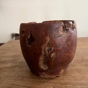 May include: A handcrafted, rustic wooden bowl with a rich, reddish-brown hue. The bowl features a unique, organic shape with visible knots and imperfections, adding to its natural charm. The bowl is approximately 6 inches in diameter and 5 inches tall.
