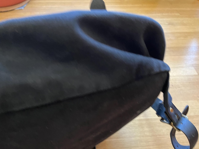 May include: Black satchel bag with a curved top and a leather strap with a brass buckle. The bag appears to be made of a soft, dark fabric.