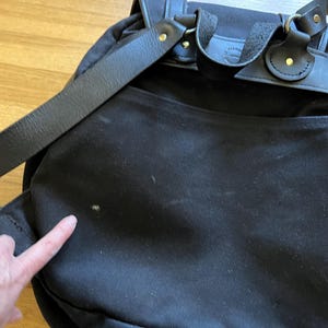May include: Black backpack with leather straps and gold-colored metal hardware. The bag has a flap closure and adjustable shoulder straps. The bag is made of a durable material and appears to be well-constructed.