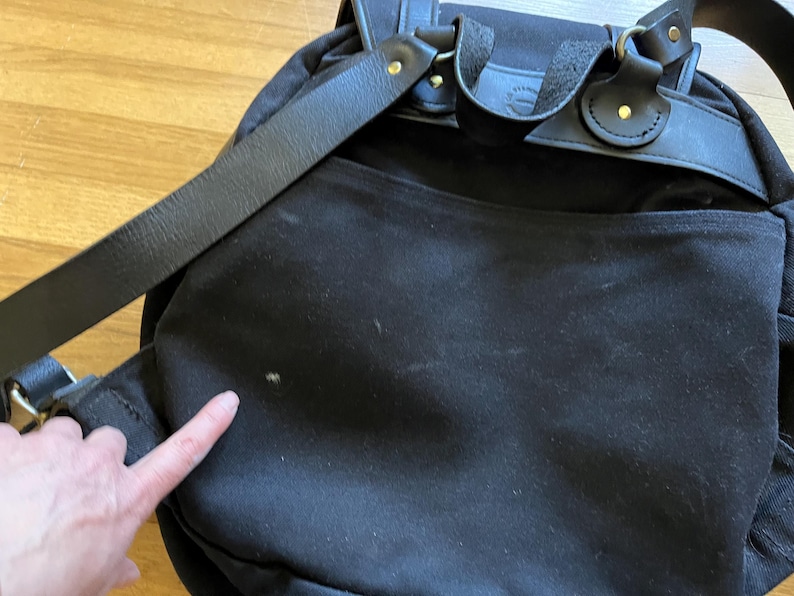 May include: Black backpack with leather straps and gold-colored metal hardware. The bag has a flap closure and adjustable shoulder straps. The bag is made of a durable material and appears to be well-constructed.