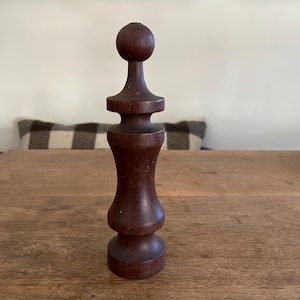 May include: A dark brown, turned-wood decorative object with a rounded top and base, and a bulbous midsection. The object is approximately 7 inches tall and stands on a wooden table.