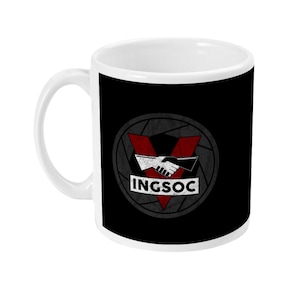 May include: White ceramic mug with a black background featuring a distressed graphic. The graphic includes a red V-shaped design, a handshake, and the word "INGSOC" in white. The mug has a white handle and interior.