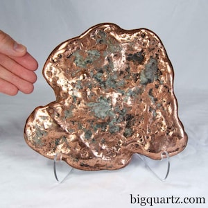 May include: A raw copper and quartz mineral specimen with a metallic, reflective copper edge and a textured, uneven surface featuring embedded white and grey quartz crystals. The piece is displayed on a clear acrylic stand with the text bigquartz.com.