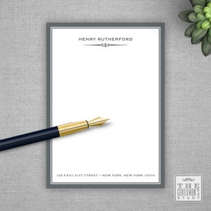 May include: Gray notepad with a white writing surface and a gray border. The notepad has the text "HENRY RUTHERFORD" at the top and the text "125 EAST 21ST STREET NEW YORK, NEW YORK 10010" at the bottom. The notepad also has a small logo with the text "THE GENTLEMAN'S STUDY" at the bottom right corner.