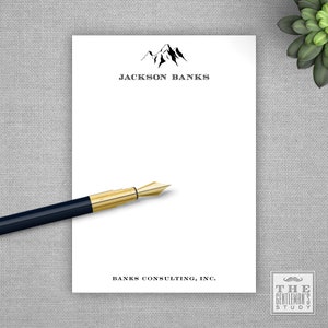 May include: White notepad with a black mountain range graphic and the text "JACKSON BANKS" at the top. The bottom of the notepad has the text "BANKS CONSULTING, INC." and a small logo that says "THE GENTLEMAN'S STUDY".