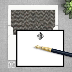 May include: A stationery set featuring a white card with a black border and a monogram, a matching envelope with a herringbone pattern, and a gold and black fountain pen. The set is from "The Gentleman's Study."