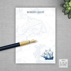 May include: A white notepad with a blue and white nautical map design. The notepad has the name "Robert Grant" printed at the top. A blue and white ship illustration is in the bottom right corner. The notepad has a gold and blue pen on top of it. The text "The Gentleman's Study" is printed in the bottom right corner.