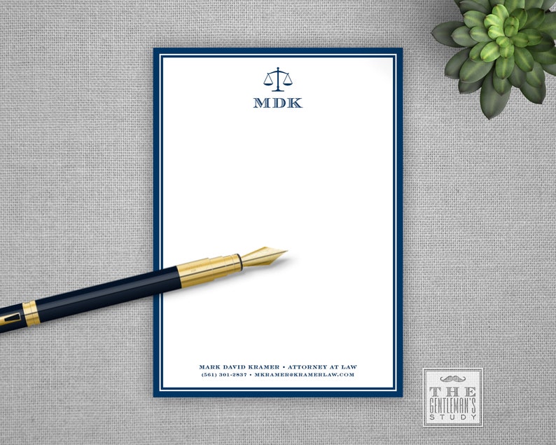 Op de afbeelding: Een wit notitieblok met een blauwe rand en een logo van een weegschaal met de initialen "MDK" gedrukt aan de bovenkant. Het notitieblok heeft een blauwe pen erop en de tekst "MARK DAVID KRAMER ATTORNEY AT LAW (561) 301-2537 MKRAMER@KRAMERLAW.COM" gedrukt aan de onderkant. De tekst "THE GENTLEMAN'S STUDY" is gedrukt in een vierkant in de rechterbenedenhoek van de afbeelding.