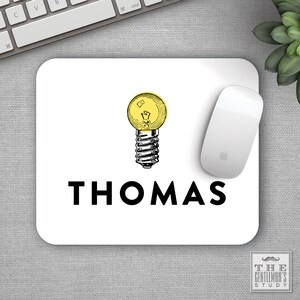 May include: White mouse pad with a black and yellow lightbulb illustration and the name "THOMAS" in black text.