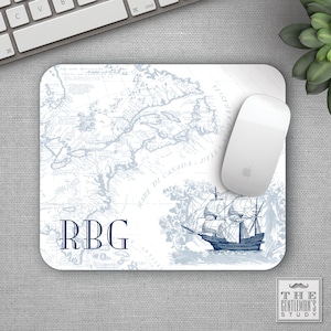 May include: A white mouse pad with a blue and white nautical map design. The map features a ship sailing on the sea. The initials "RBG" are printed in blue in the lower left corner. The mouse pad is designed by The Gentleman's Study.