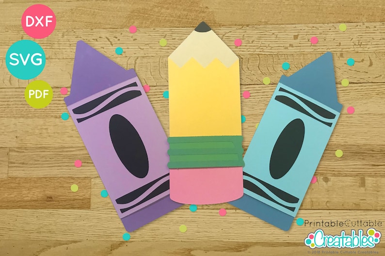 May include: Three printable cut-out shapes of school supplies: a purple crayon, a yellow pencil, and a blue crayon. The shapes are on a woodgrain background with colourful confetti.